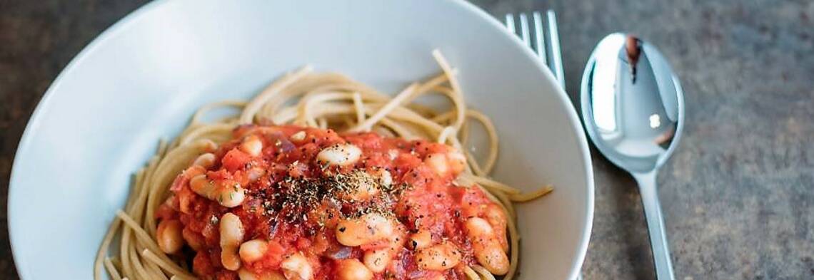 Teller mit Spaghetti und weißen Bohnen, daneben Besteck von oben fotografiert