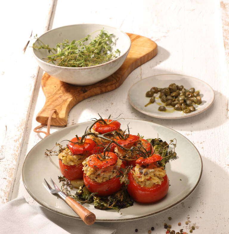 Gefüllte Tomaten auf weißem Teller mit Salat und Kapern auf kleinem Teller