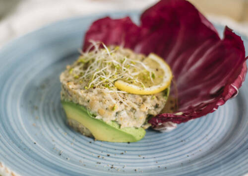 Veganer Thunfischsalat auf einem blauen Teller mit Avocado und Radicchio, von vorne fotografiert.