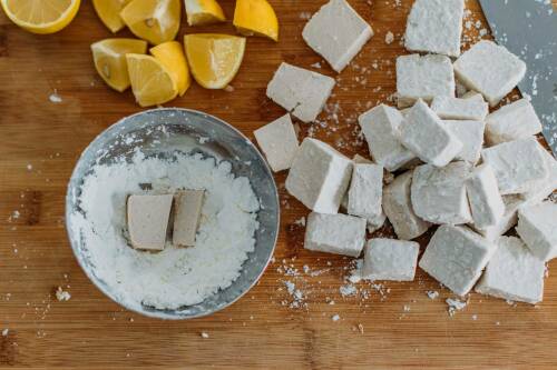 Tofu in Stärke auf Schneidebrett neben Zitronen.