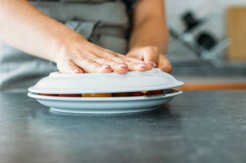 Schritt 3: Während man den oberen Teller fixiert, schneidet man mit der anderen Hand zwischen den Tellern durch, um Tomatenhälften zu erhalten.