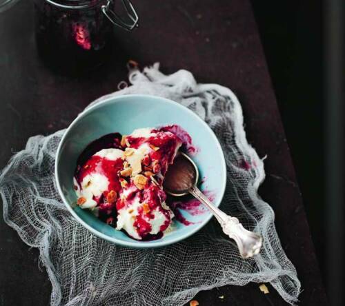 Vanilleeis in blauer Schüssel mit Erdbeersoße vor dunklem Hintergrund.