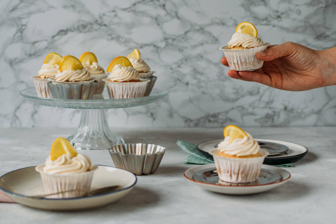 Vegane Cupcakes mit Zitrone auf Tellern und Hand vor hellem Hintergrund.
