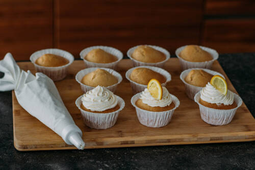 vegane Cupcakes  mit Frosting und Zitronen neben Spritzbeutel vor dunklem Hintergrund.