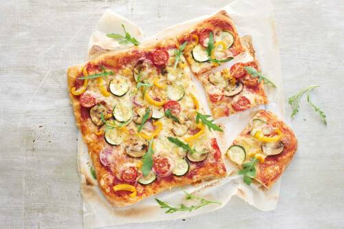 Vegane Gemüsepizza von Simply V auf Backpapier vor hellem Hintergrund.