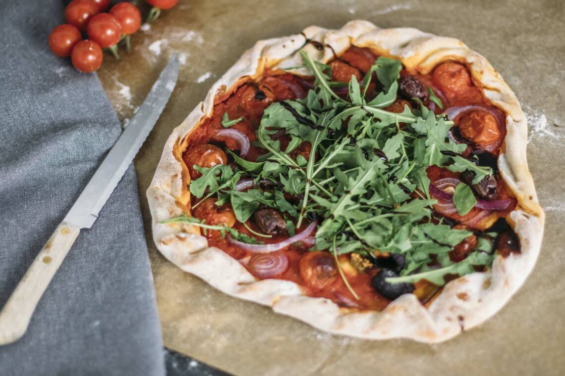 Vegane Pizza aus Bierteil auf Backpapier, daneben frische Tomaten