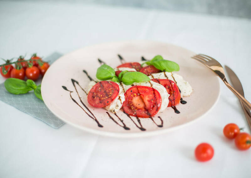 Veganer Mozzarella mit Tomaten und Balsamico auf einem Teller. Von der Seite fotografiert.