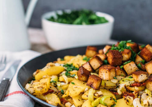 Veganes Kartoffel-Gröstl mit knusprigen Tofu-Würfeln. Von der Seite fotografiert.