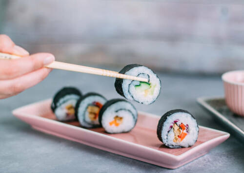 Frisch gerolltes Sushi wird mit Stäbchen vom Teller angehoben.