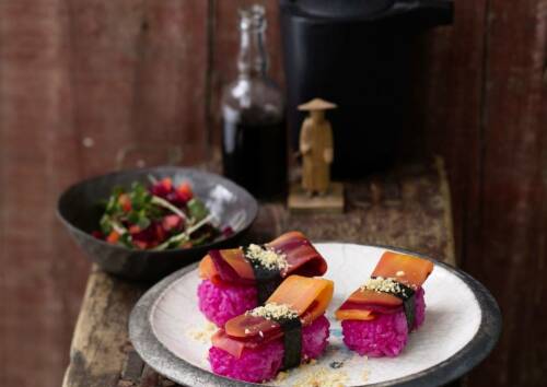 Veggie-Nigiri mit pinken Reis auf einem Teller, von vorne fotografiert.