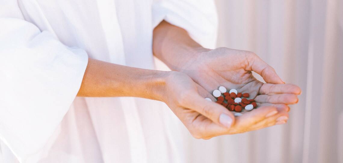 Frau hält verschiedene Tabletten in ihren beiden Händen, die sie zu einer Schale geformt hat. Der Hintergrund ist weiß.