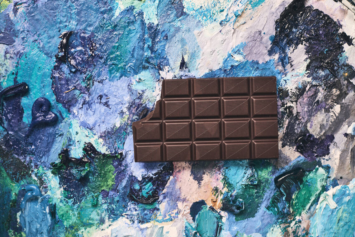 Eine Tafel Schokolade, von der ein Stück abgebrochen wurde, auf künstlerischem vielfarbigem Hintergrund.