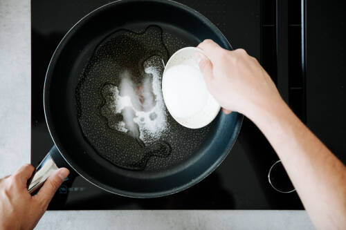 Zucker wird in eine Pfanne mit Wasser geschüttet, um ihn zu karamellisieren.