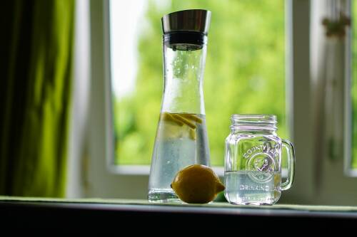 Viel Wasser zu trinken ist beim gesunden Abnehmen sehr wichtig. Hier sieht man eine Karaffe mit Wasser und Zitronenscheiben gefüllt, daneben ein halb gefülltes Glas.