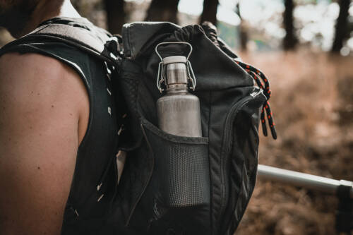 Eine Wasserflasche aus Edelstahl steckt in einem Rucksack, den ein Mann auf einer Wanderung trägt.