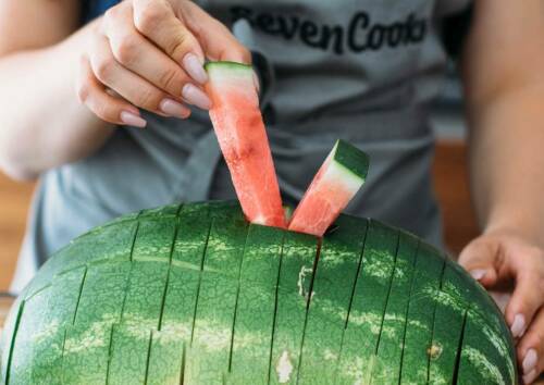 Wassermelone in Sticks geschnitten, zwei Sticks werden herausgezogen.
