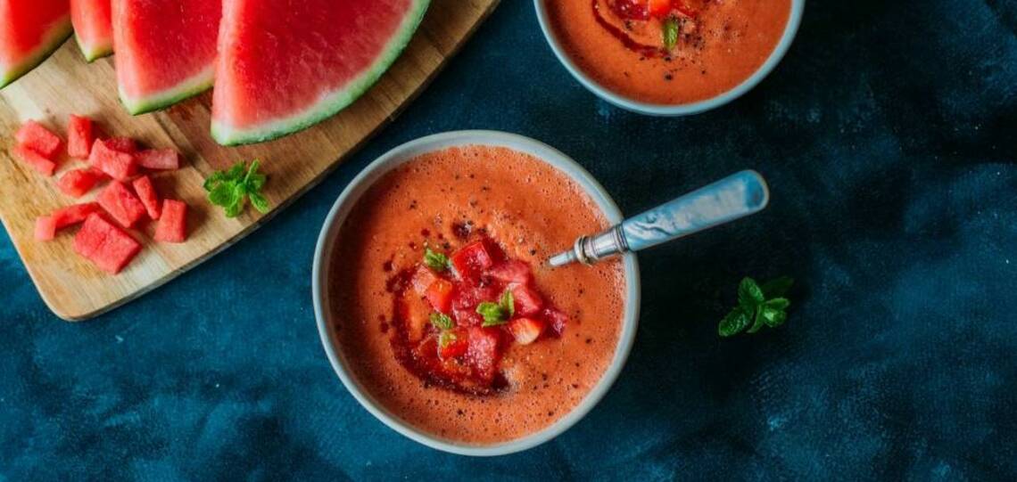 Schüssel gefüllt mit roter Gazpacho von der Wassermelone, Tomate und Paprika, vor dunkelblauem Hintergrund. Von oben fotografiert.