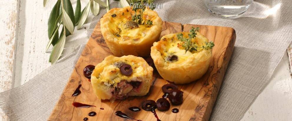 Käsemuffins auf Holzbrett mit Kirchen und Oliven