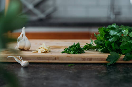 Zubereitung_Schritt_2:_Knoblauch_in_Scheiben,_Petersilie_hacken Zubereitung: Knoblauch in Scheiben, Petersilie hacken auf Holzbrett